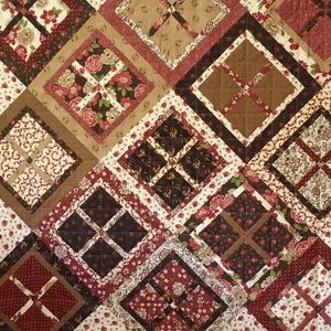 May include: A quilt with a diamond pattern in shades of brown, red, and cream. The quilt is made of various fabrics with floral and geometric designs.