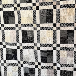 May include: A handmade quilt with a geometric pattern in black, white, and gray. The quilt features a grid design with alternating squares of solid and patterned fabrics. The border is a solid gray fabric.