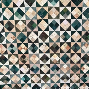 May include: A quilt with a diamond pattern in shades of green and beige. The quilt is made up of many smaller squares, each with a different pattern. The quilt is framed with a dark green border.