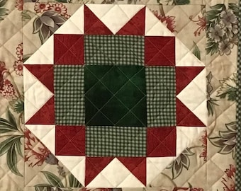 May include: A quilted table runner with a floral pattern in shades of green, brown, and cream. The runner features three red and white star-shaped blocks with a green and white checkered center.