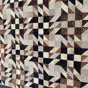 May include: A quilt made of various brown and beige fabrics with animal print patterns. The quilt is made up of squares and triangles, and the seams are outlined in black thread.
