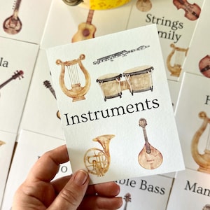 Könnte beinhalten: Eine weiße rechteckige Lernkarte mit Aquarellillustrationen einer Leier, einer Flöte, Bongos, einem Waldhorn und einer Mandoline. Das Wort Instruments ist in schwarzer Schrift in der Mitte der Karte gedruckt, umgeben von weiteren Karten.