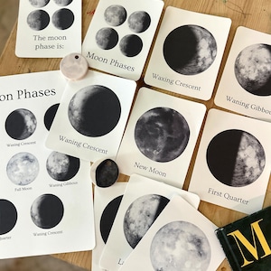 Könnte beinhalten: Eine Sammlung weißer Lernkarten mit schwarz-weißen Illustrationen verschiedener Mondphasen. Jede Karte zeigt eine bestimmte Phase des Mondzyklus mit dem entsprechenden Namen in schwarzer Schrift, wie Waxing Crescent, Waning Gibbous, New Moon, First Quarter und Full Moon.