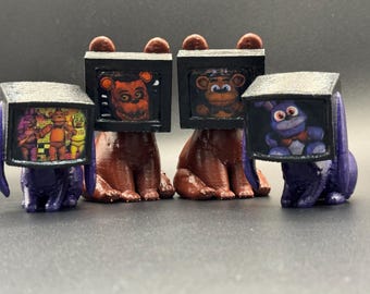 May include: Four figurines of characters from the video game Five Nights at Freddy's. Two are brown bears with television screens for heads, and two are purple rabbits with television screens for heads. The screens display images of the characters.