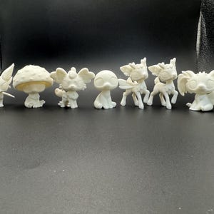 May include: A collection of small, off-white figurines of various creatures, including a fox, mushroom, elephant-like figure, and deer-like animals. The figurines are arranged in a row against a dark background, showcasing their unique designs and forms.