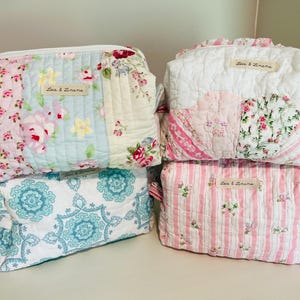Puede incluir: Cuatro neceseres acolchados con diseños florales y estampados. Las bolsas presentan telas rosas, azules y blancas con estampados florales y a rayas. Cada bolsa tiene cierre de cremallera y una etiqueta que dice "Lace & Linens."