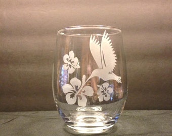 May include: A clear glass wine glass with an etched design of a hummingbird and hibiscus flowers.