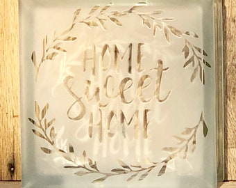 May include: A frosted glass block with a white etched design of a leafy wreath and the text "Home Sweet Home".