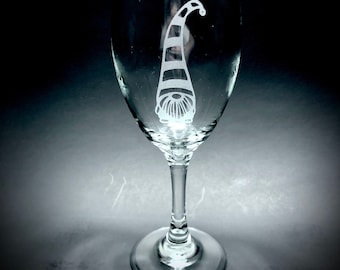 May include: A clear glass wine glass with a white etched design of a gnome with a striped hat.