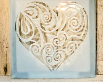 May include: A frosted glass block with a white etched heart design. The heart is filled with intricate swirls and patterns.