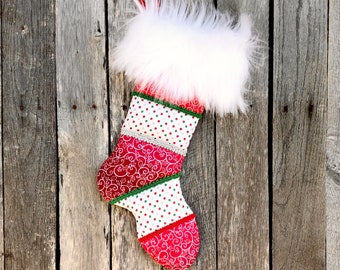 May include: A handmade Christmas stocking with a white faux fur cuff and a red hanging loop. The body features red and white patterned fabric with green and silver trim. The stocking is hanging against a weathered wooden background.