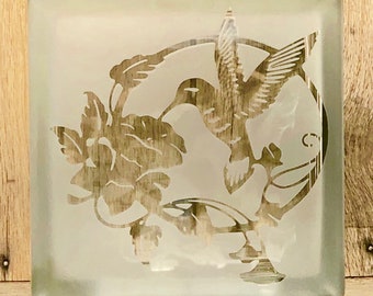 May include: A frosted glass block with an etched design of a hummingbird in flight, surrounded by flowers and leaves.