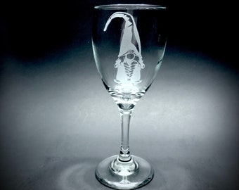 May include: A clear glass wine glass with a gnome etched into the side. The gnome is facing forward with its arms crossed and a hat on its head.