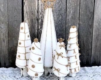 May include: A collection of five white decorative Christmas trees of varying sizes. The trees are adorned with jute rope, twine, and star accents. The trees are set against a rustic wooden background and a white lace tablecloth.