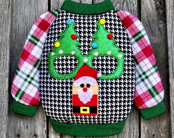May include: A festive Christmas sweater with a black and white houndstooth pattern. The sweater features green Christmas tree glasses and a Santa Claus applique. The sleeves have a red and white plaid design, and the collar and cuffs are green.