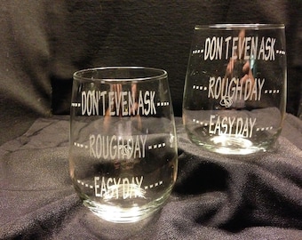 May include: Two clear glass wine glasses with the text "Don't even ask... Rough day... Easy day..." etched on them.