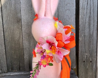 May include: A pink fluffy bunny rabbit with a large orange bow and pink, orange, and yellow flowers.
