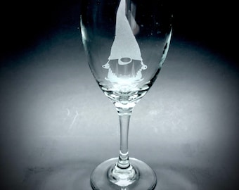 May include: A clear glass wine glass with a white etched design of a gnome wearing a pointed hat.