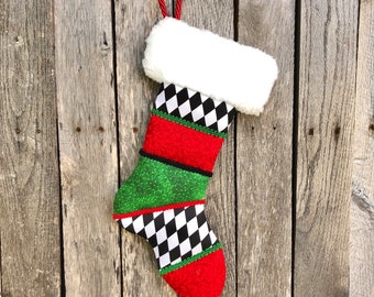 May include: A Christmas stocking with a white faux fur cuff and a red and green body. The stocking features a black and white checkered pattern, red and green patterned fabric, and a red hanging loop.