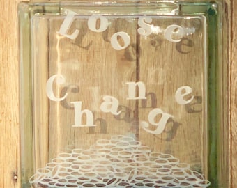 May include: A clear glass block with the words "Loose Change" etched on the front. The block is filled with a pile of coins, represented by a white outline.