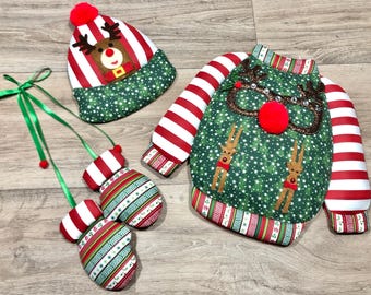 May include: A festive Christmas-themed set featuring a green sweater with reindeer and a red nose, a matching hat, and two mittens. The sweater and hat have red and white striped accents. The mittens are connected by a green ribbon.