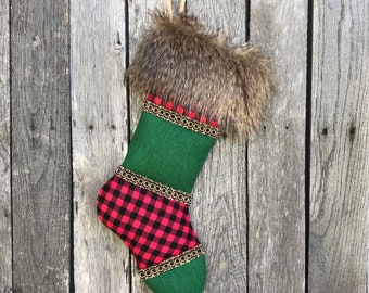 May include: A Christmas stocking with a faux fur cuff and a green body. The toe and heel are red and black buffalo plaid. Gold trim with red accents borders the green section. A loop of twine is attached for hanging.