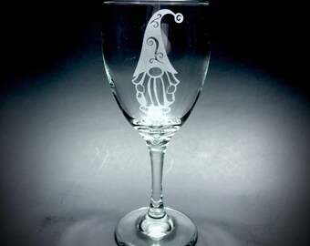 May include: A clear glass wine glass with an etched design of a gnome with a pointed hat.