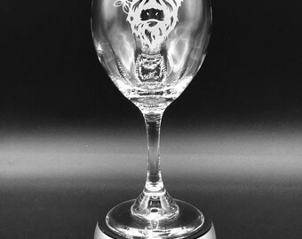 May include: A clear glass wine glass with a white etched design of a Highland cow wearing a flower crown. The glass is sitting on a silver base.