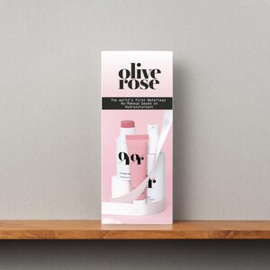 May include: A gift set of Olive Rose skincare products. The packaging is a tall, rectangular box with a gradient pink background. The text "olive rose" is at the top. The set includes several white and pink bottles and tubes, with a white ribbon.
