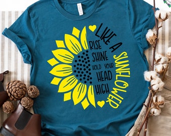 May include: A teal blue t-shirt with a yellow sunflower graphic and the text "Like a Sunflower, Rise Shine Hold Your Head High".