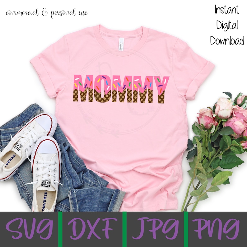Puede incluir: Camiseta rosa con la palabra "MOMMY" en letras marrones y rosas con chispas en la parte superior. Las letras est&aacute;n dise&ntilde;adas para parecer conos de helado. La camiseta est&aacute; sobre un fondo blanco con un par de pantalones vaqueros azules y zapatillas blancas.