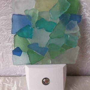 K&ouml;nnte beinhalten: Ein wei&szlig;es Nachtlicht mit einem Mosaik aus Meerglas in Blaut&ouml;nen, Gr&uuml;n- und Wei&szlig;t&ouml;nen. Das Meerglas ist in einem zuf&auml;lligen Muster angeordnet und wird vom Licht beleuchtet.