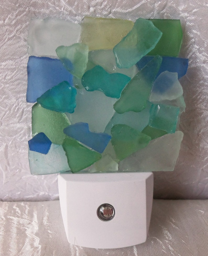 K&ouml;nnte beinhalten: Ein wei&szlig;es Nachtlicht mit einem Mosaik aus Meerglas in Blaut&ouml;nen, Gr&uuml;n- und Wei&szlig;t&ouml;nen. Das Meerglas ist in einem zuf&auml;lligen Muster angeordnet und wird vom Licht beleuchtet.