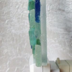 K&ouml;nnte beinhalten: Ein Nachtlicht mit einem Mosaik aus blauen, gr&uuml;nen und wei&szlig;en Glasst&uuml;cken. Das Licht ist an einem wei&szlig;en Stecker befestigt.