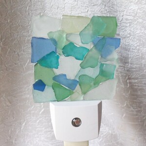 K&ouml;nnte beinhalten: Ein wei&szlig;es Nachtlicht mit einem Mosaik aus blauem, gr&uuml;nem und klarem Meerglas. Das Nachtlicht hat einen runden, wei&szlig;en Knopf an der Seite.