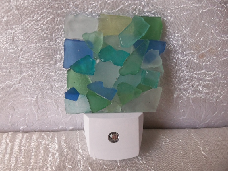 K&ouml;nnte beinhalten: Ein wei&szlig;es Nachtlicht mit einem klaren Glasschirm, der mit einem Mosaik aus blauen, gr&uuml;nen und wei&szlig;en Meerglassplittern verziert ist.