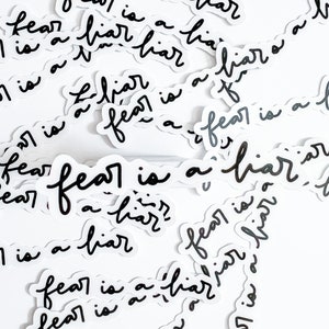 May include: A collection of black and white stickers with the text "fear is a liar" repeated multiple times. The stickers are scattered on a white background.