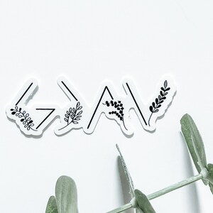 May include: A white sticker with the word "God" written in black with arrows pointing up and down. The sticker has small black floral designs around the word.