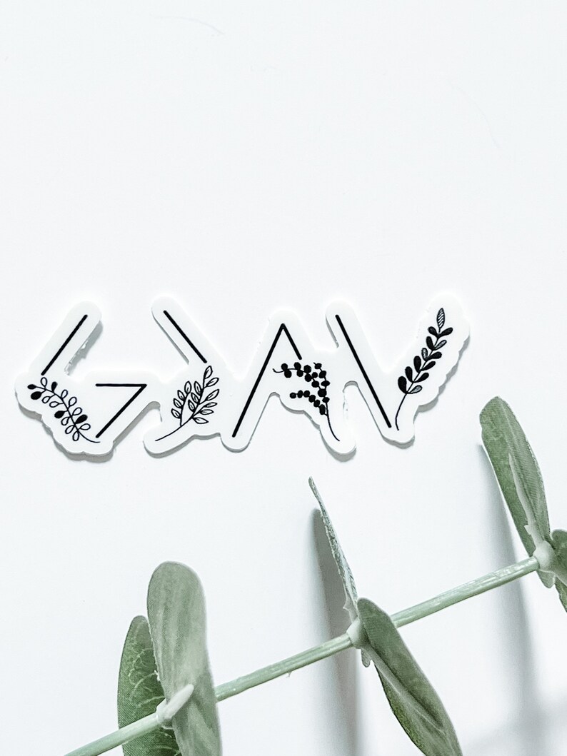 May include: A white sticker with the word "God" written in black with arrows pointing up and down. The sticker has small black floral designs around the word.