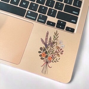 May include: A sticker of a bouquet of flowers with orange, purple, and green leaves on a gold laptop.