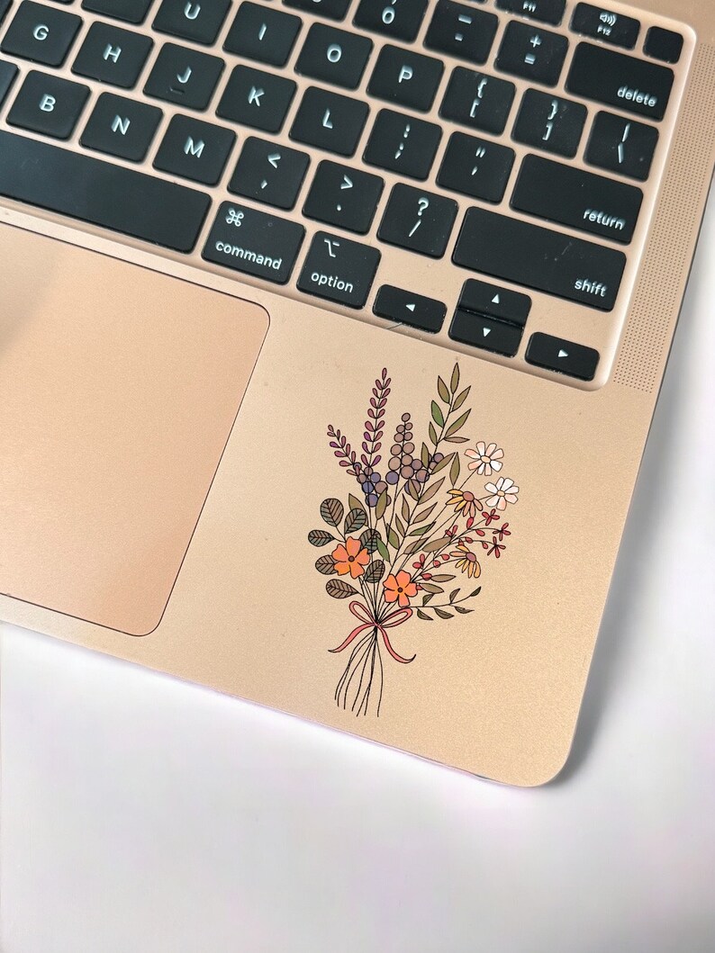 May include: A sticker of a bouquet of flowers with orange, purple, and green leaves on a gold laptop.