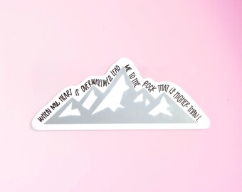 May include: A sticker in the shape of a mountain range with the text "WHEN MY HEART IS OVERWHELMED, LEAD ME TO THE ROCK THAT IS HIGHER THAN I." The sticker is white and gray, set against a pink background.