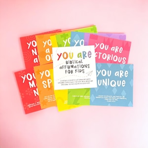May include: A set of colorful affirmation cards with the text "You Are" and a biblical verse on each card. The cards are designed for kids and feature a rainbow color scheme.