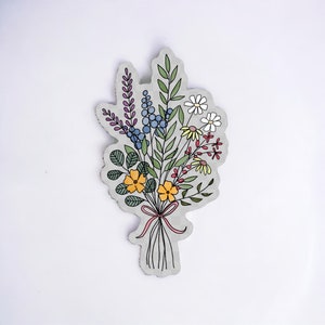 May include: A hand-drawn illustration of a bouquet of flowers with a pink ribbon. The flowers are in shades of blue, yellow, and red.