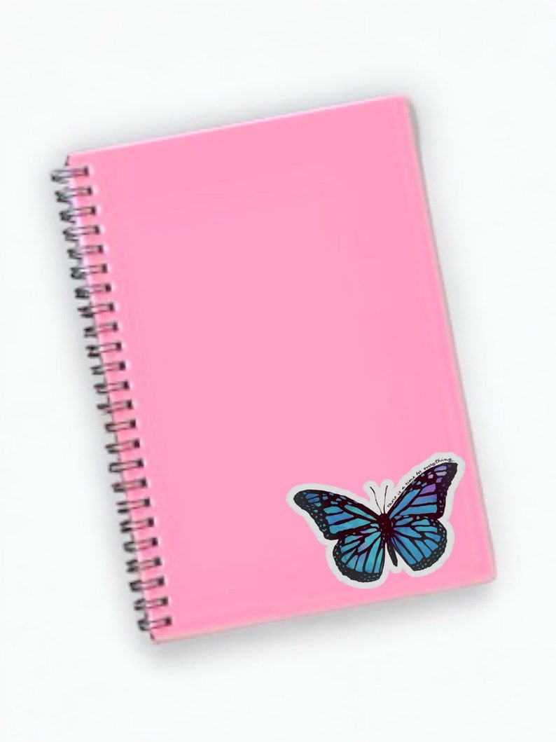 May include: A pink spiral bound notebook with a blue butterfly sticker on the cover. The butterfly sticker has the text "This is my everything" on it.