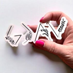 May include: White sticker with black arrows pointing upwards and small black floral designs. The sticker says "<3" in the centre.
