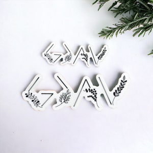 May include: Two white wooden signs with black floral designs and the word "God" written in black arrows. The signs are on a white background.