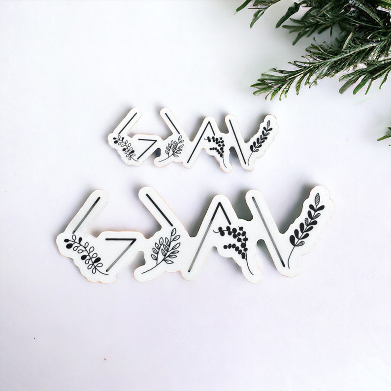 May include: Two white wooden signs with black floral designs and the word "God" written in black arrows. The signs are on a white background.