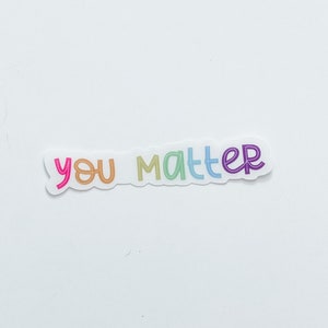 Op de afbeelding: Een witte sticker met de tekst "you matter" in regenboogkleuren.