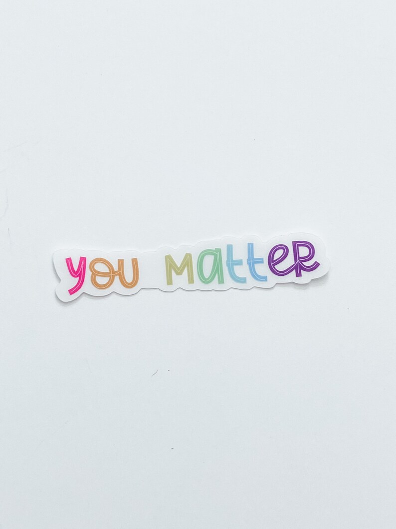 Op de afbeelding: Een witte sticker met de tekst "you matter" in regenboogkleuren.